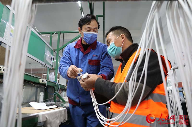 2月28日，在慈溪市萬能電子有限公司，來自貴州黔西南布依族苗族自治州的馬德富（右一）在同事劉奎的指導下檢驗產品外觀。章勇濤 攝