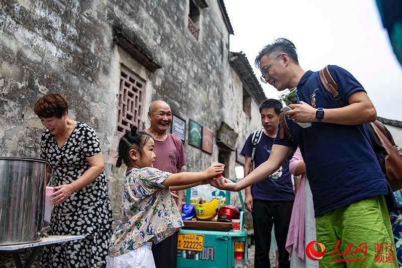 7月17日，童鬆達老人（左二）帶著曾孫女周予童來到附近的前童古鎮景區，為游客送上一杯茶。章勇濤 攝