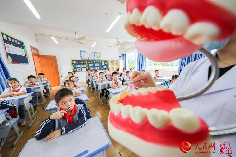 9月17日，在浙江省湖州市德清县武康街道东风小学，一名牙科医生借助牙齿模型为学生们讲解牙齿保健知识。