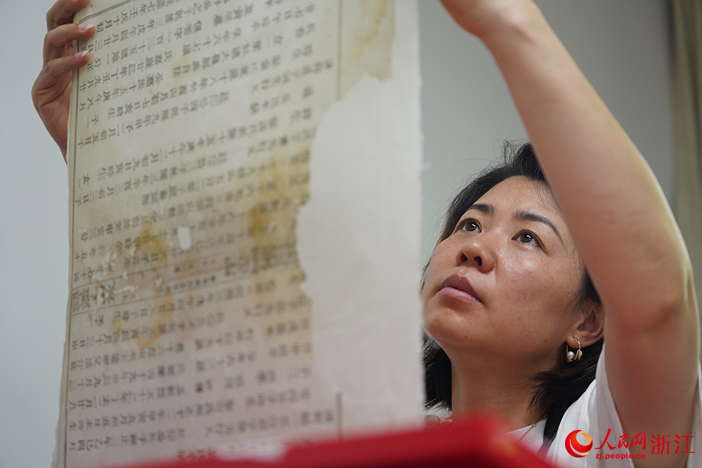古籍修复师拿起古籍书叶查看破损情况。人民网 章勇涛摄