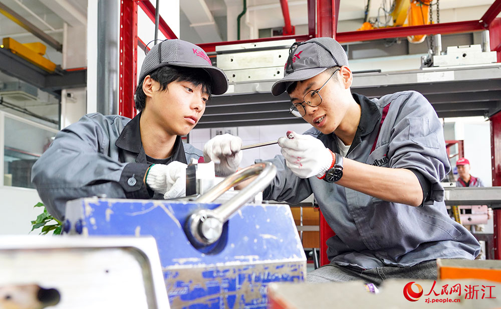 在台州科技职业学院凯华模具产业学院，高级钳工余叶敏（右）在指导学生对模具滑块进行丝攻操作。人民网 章勇涛摄