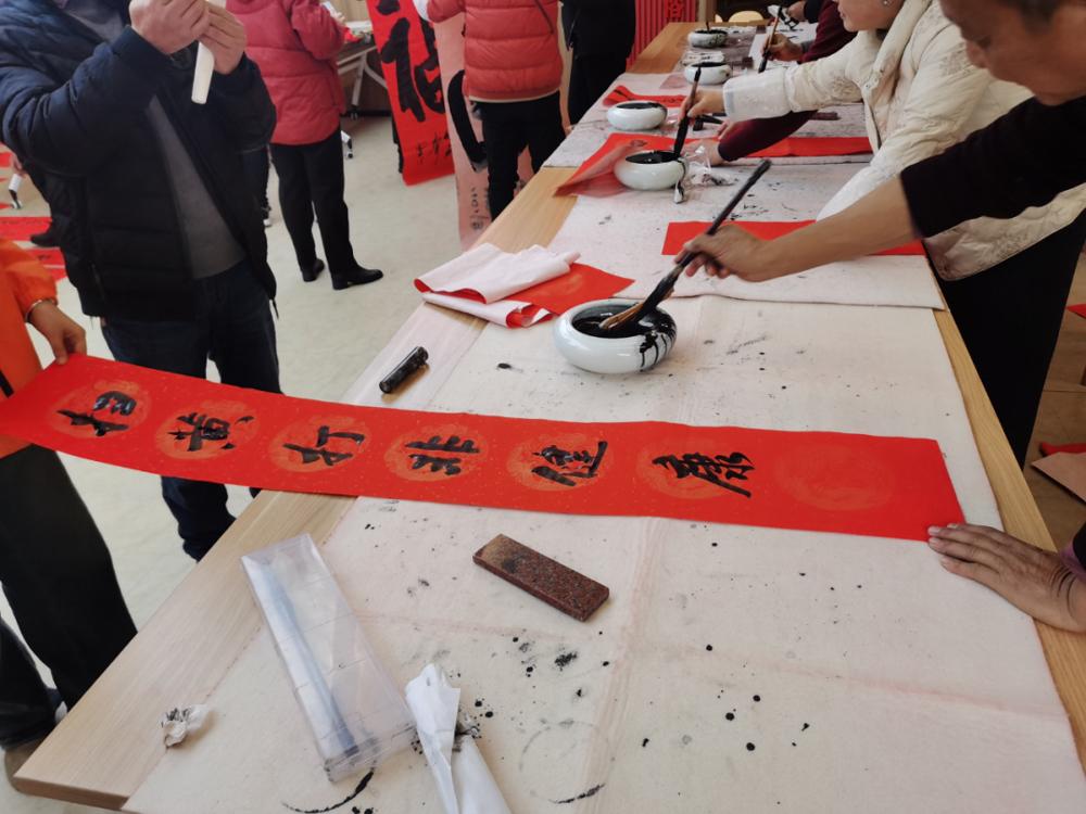 在嵊州仙岩镇组织的写春联送祝福活动现场，书法爱好者们将一幅幅关于“扫黄打非”和版权保护主题的春联赠给群众。嵊州市委宣传部供图