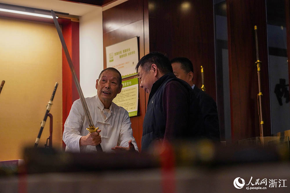 在浙江省龙泉市沈广隆剑铺,沈新培(左)在向来自山东的客人介绍龙泉宝剑。人民网 章勇涛摄