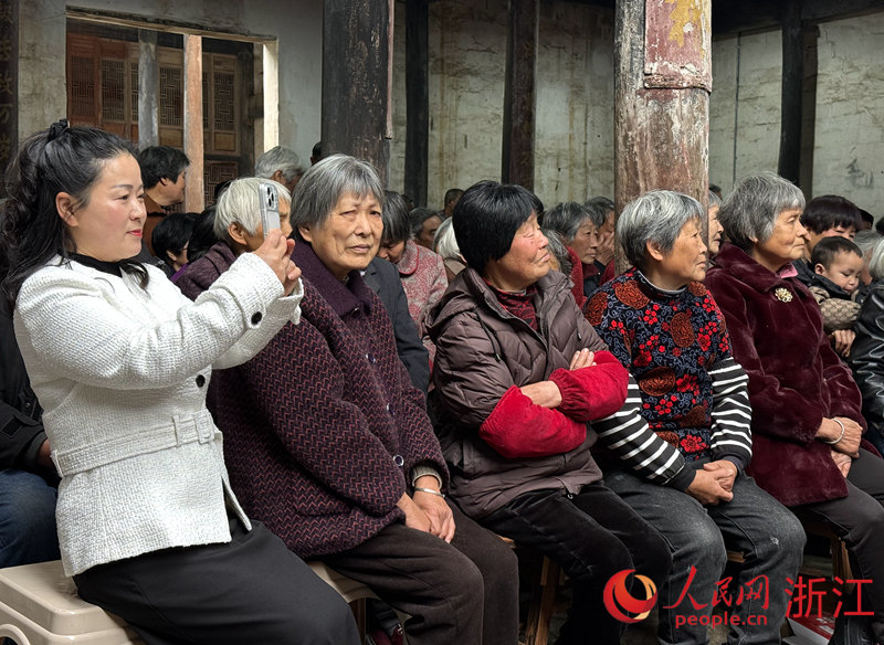 郑飞（左一）坐在台下听戏、拍摄。人民网记者 方彭依梦摄